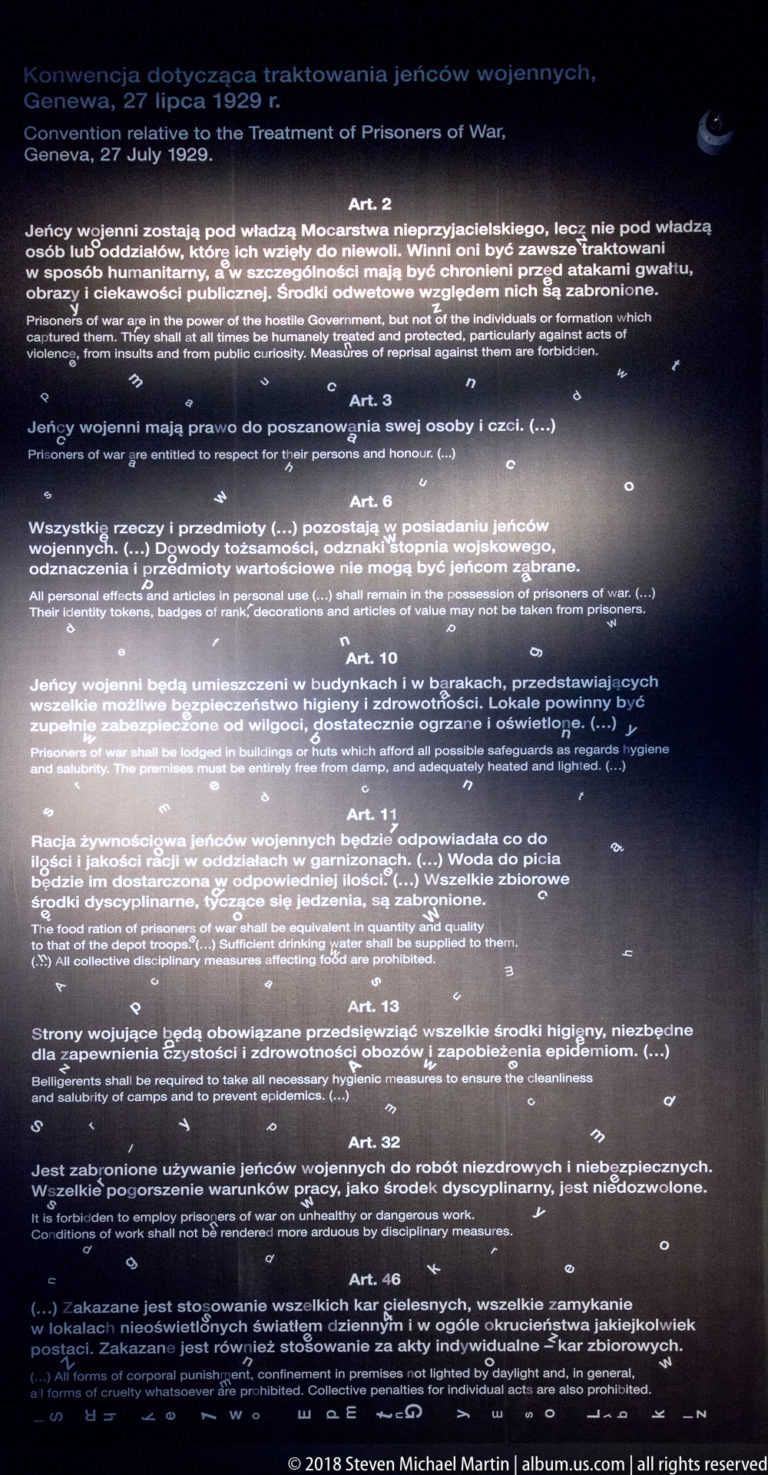 Large illuminated wall filled with Polish legal text divided into numbered articles in a dark gallery.