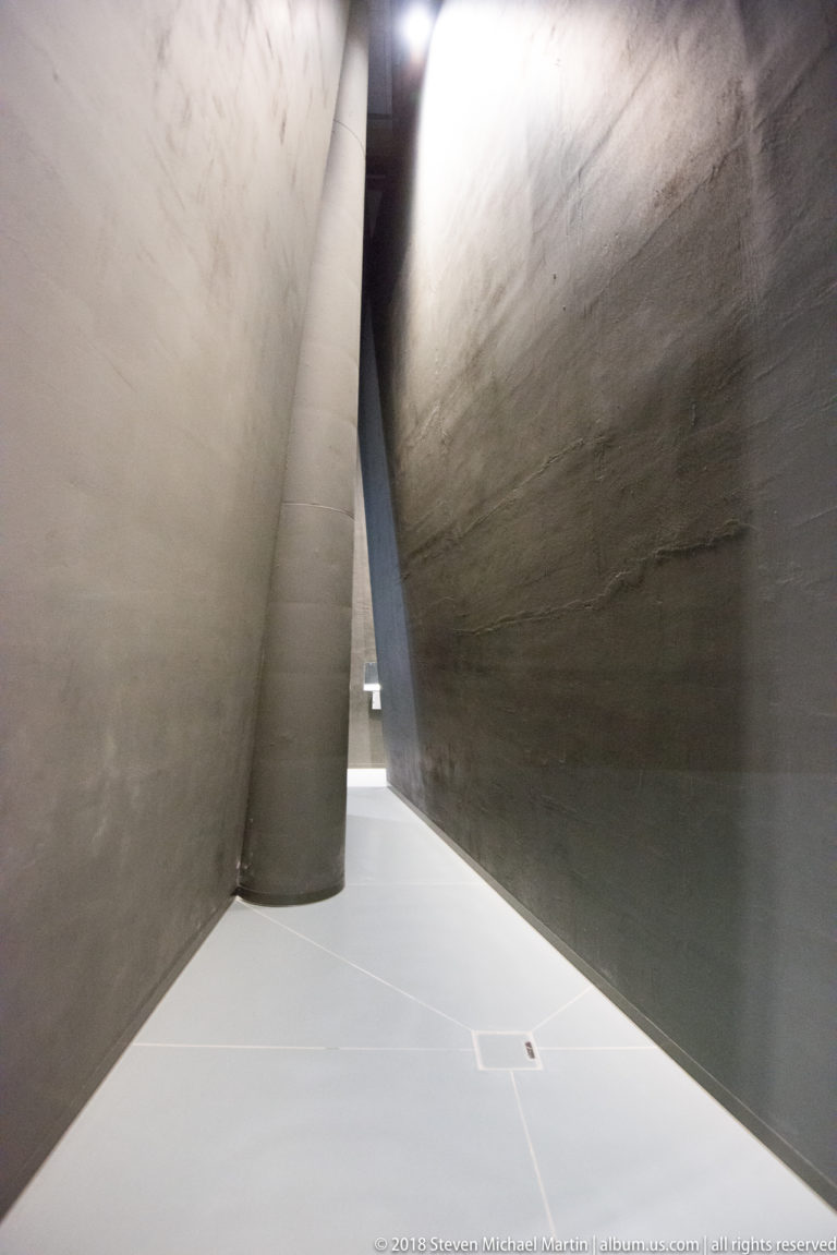 Bright narrow passage between massive sloping raw-concrete walls inside the museum.