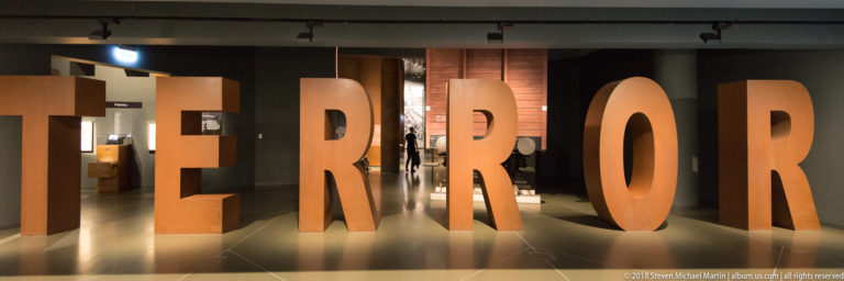 Large rust-colored freestanding letters spelling TERROR across a museum gallery entrance.