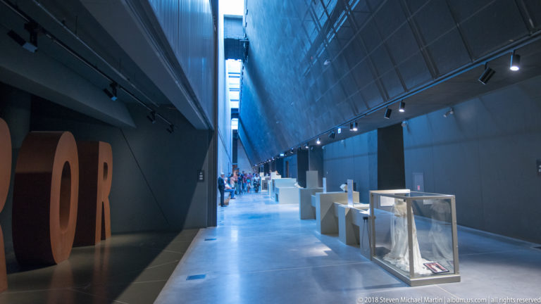 Long modern museum corridor with glass display cases and the edge of large TERROR lettering at left.