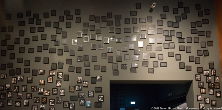 Large gray wall covered with many small framed family photographs clustered around dark door openings.