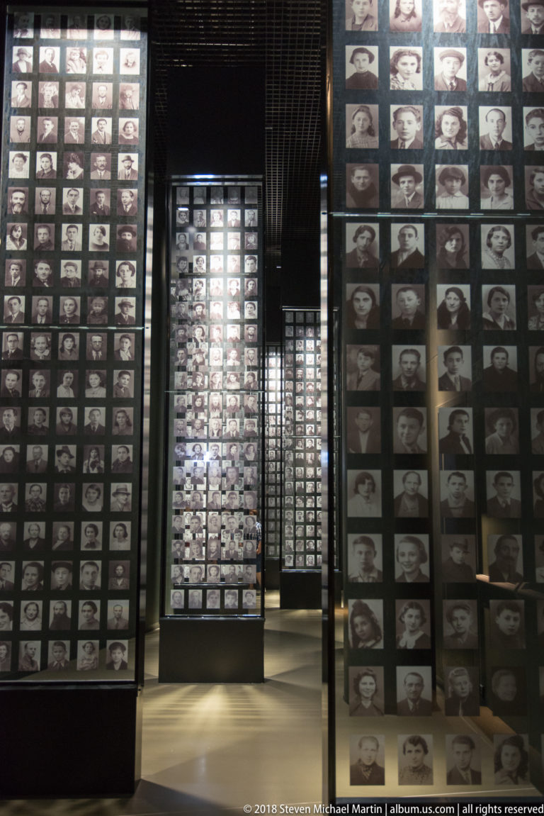 Tall black panels covered with grids of historical black-and-white portrait photographs in a museum passage.