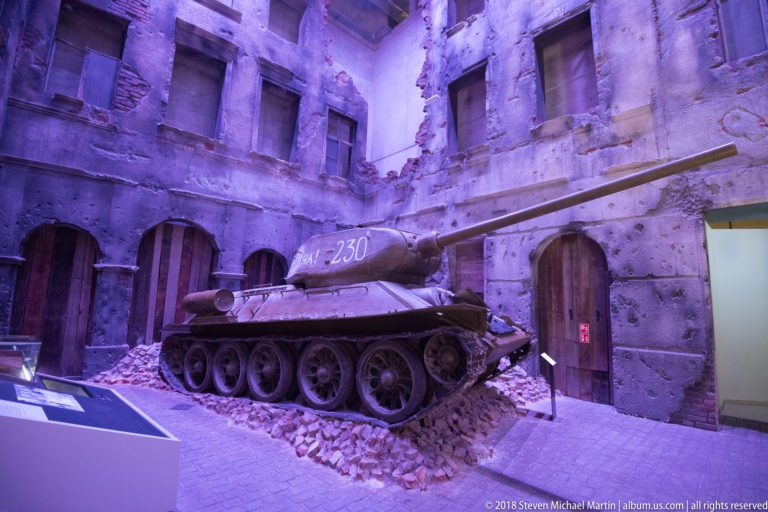 Tracked Soviet tank displayed amid rubble and reconstructed war-damaged building façades inside the museum.