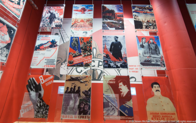 Large angled display covered with Soviet propaganda posters, including portraits of Stalin and bold red political graphics.