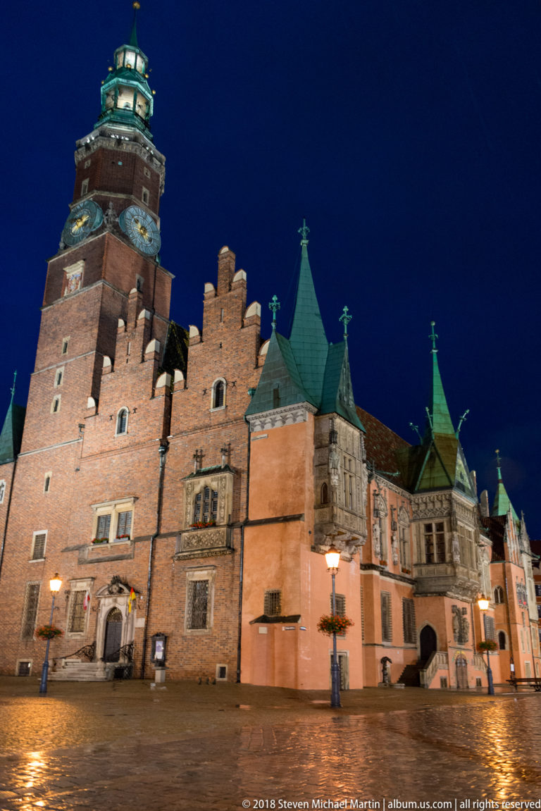 Low-angle night view of Wrocław Old Town Hall with brick tower, crenellations, and green copper rooflets.