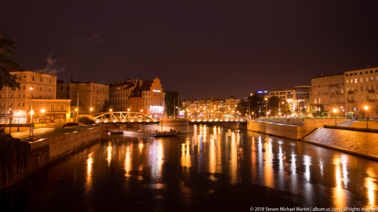 Night view along the Odra with illuminated embankments, buildings, and golden reflections on the river.