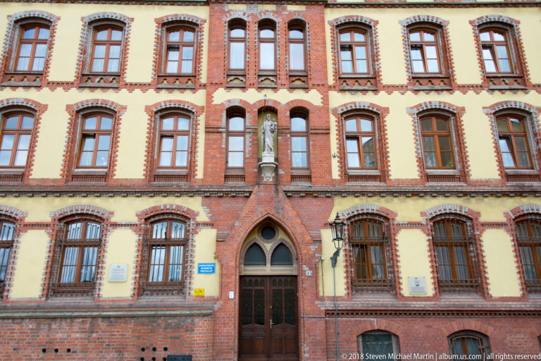 Symmetrical red-and-cream brick façade with pointed doorway, niche statue, tall windows, and decorative masonry.