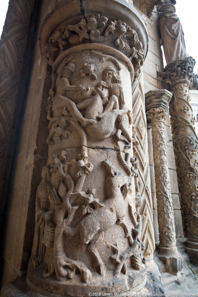 Close view of weathered carved stone packed with intertwined figures, animals, foliage, and decorative bands.