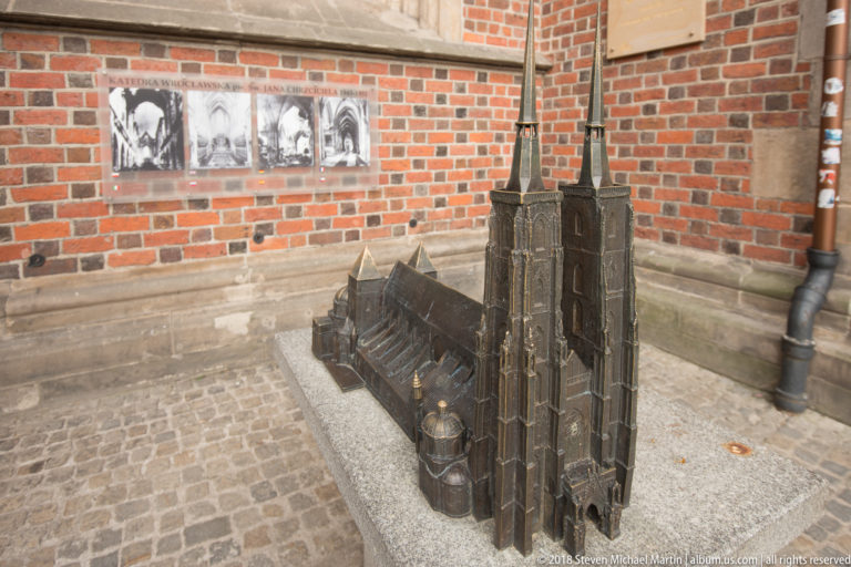 Bronze architectural model of a large twin-towered Gothic cathedral displayed beside archival photographs.