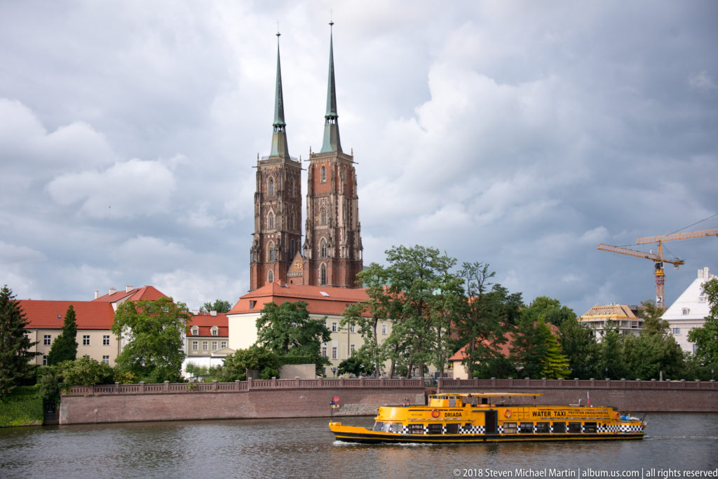 Wrocław Cathedral’s twin towers rise across the Oder as a yellow passenger boat moves along the river.