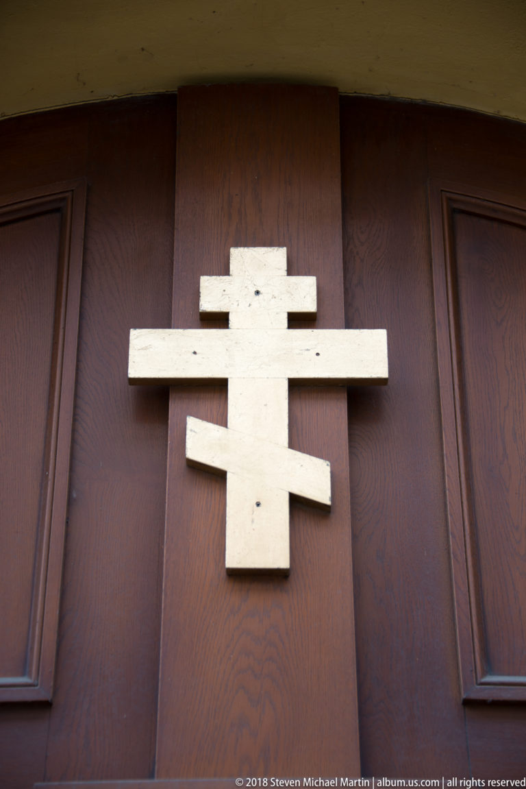 Pale multi-barred Eastern Christian cross mounted on a dark wooden door.