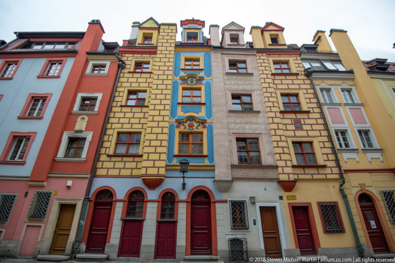 Colorful narrow townhouses with painted masonry patterns, blue window trim, decorative scrollwork, and red doors.