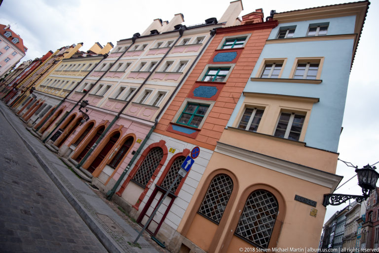 Oblique view along colorful narrow historic façades with arched ground-floor openings and closely spaced windows.