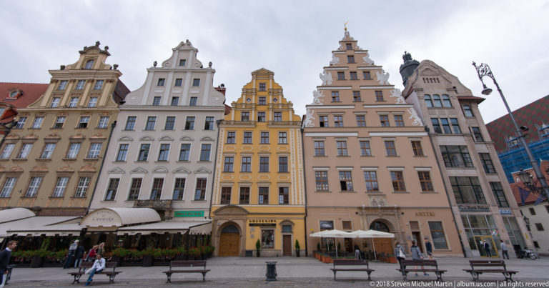 Row of narrow pastel townhouses with ornate gables and ground-floor cafés on Wrocław Market Square.