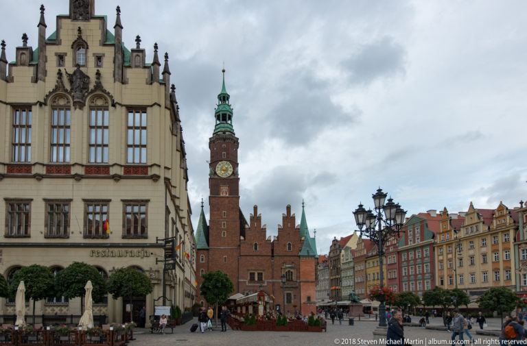Wrocław Old Town Hall and clock tower framed by ornate market-square buildings beneath a cloudy sky.