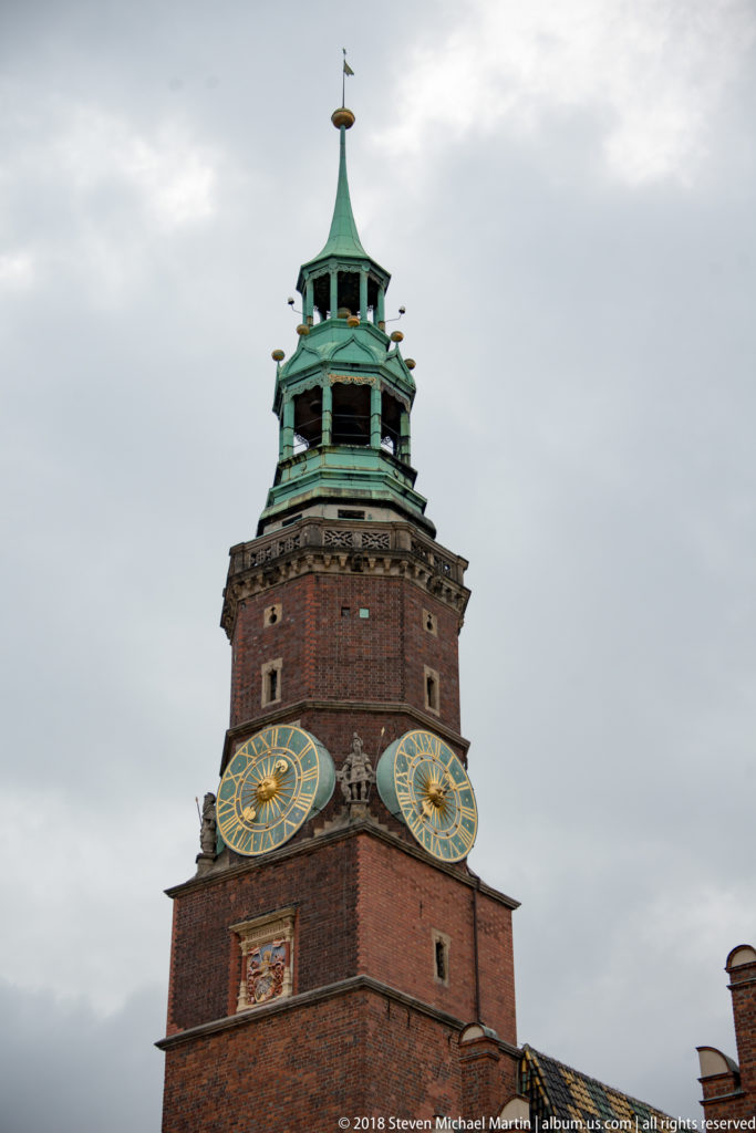 Close view of Wrocław Old Town Hall tower with two clock faces, brick masonry, and green copper lantern.