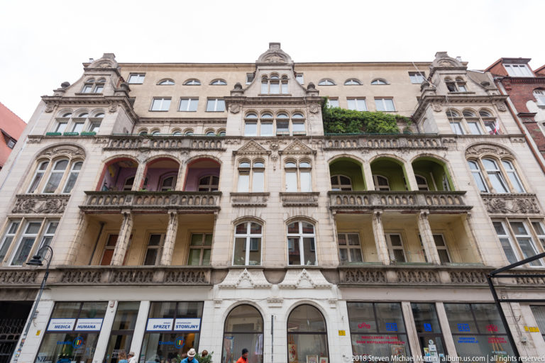 Ornate pale multistory façade with carved details, arched windows, projecting bays, and colorful recessed balconies.