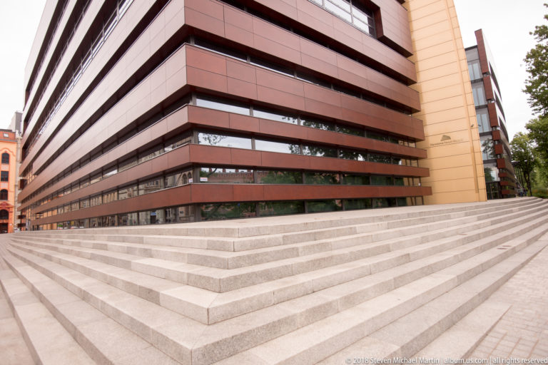 Wide stone steps rise beside a modern building with horizontal reddish bands and dark strip windows.