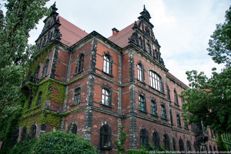 Red-brick historic institutional building with dark stone trim, ornate stepped gables, arched windows, and ivy.