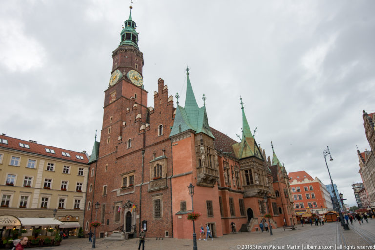 Wide view of Wrocław Old Town Hall with tall brick clock tower, stepped gables, and green copper roofs.