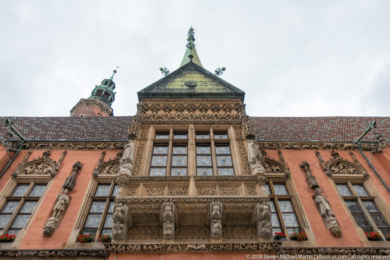 Ornately carved stone bay with tall windows and small sculptures projecting from the red-brick Old Town Hall.