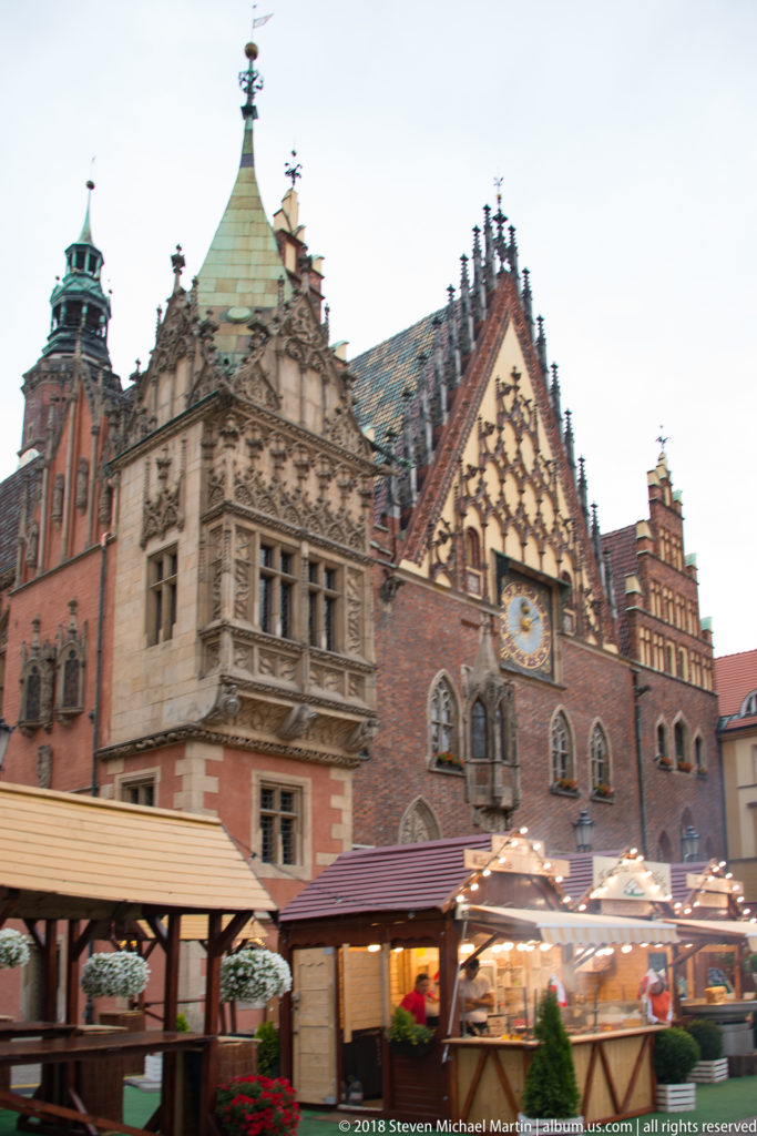 Oblique view of Wrocław Old Town Hall above market stalls, showing steep roofs, turrets, gables, and clock.