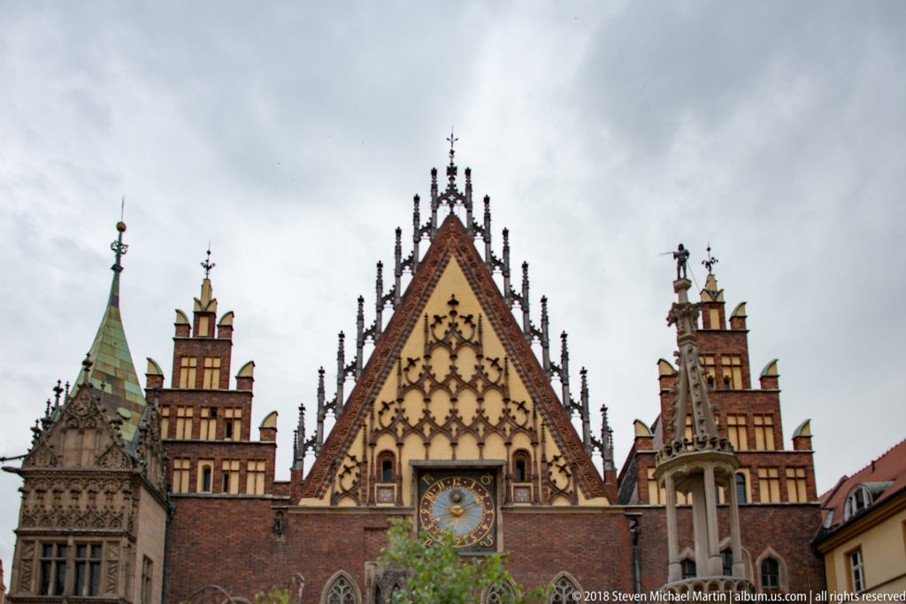 Steep decorated brick gable of Wrocław Old Town Hall with astronomical clock, pinnacles, and flanking towers.