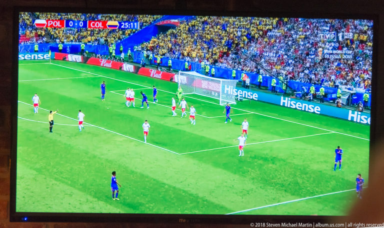 Television showing an international football match with a white-and-red team defending near the goal.