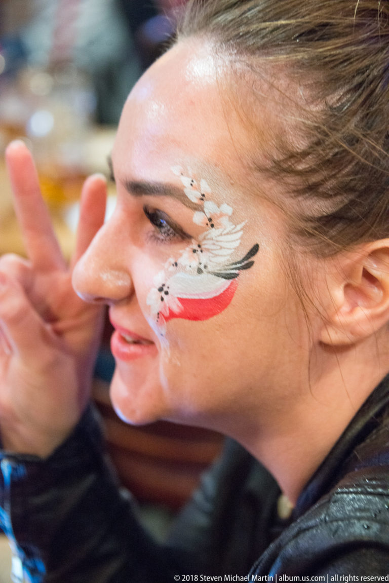Close portrait of a woman with Polish white-and-red face paint and a white eagle motif on her cheek.
