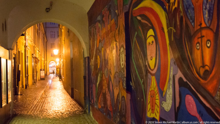 Narrow cobbled Wrocław alley at night with colorful graffiti murals along one wall and a lit archway ahead.