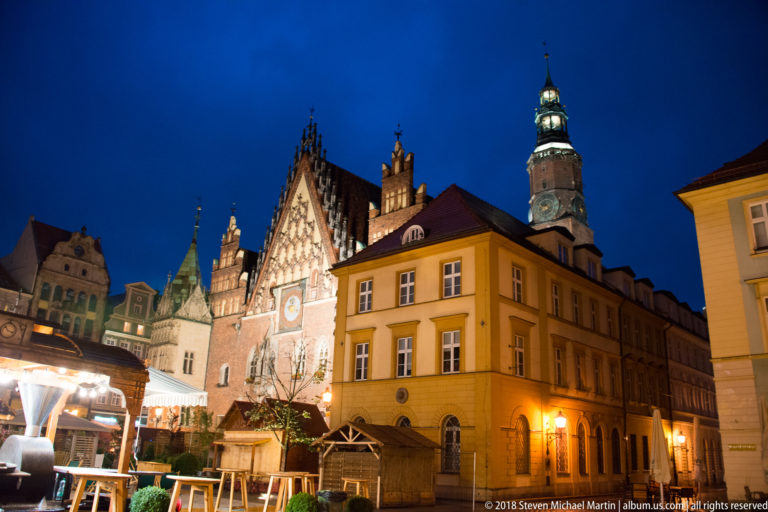 Old Town Hall gable and tower rising behind a yellow corner building and market stalls on Wrocław’s Rynek.