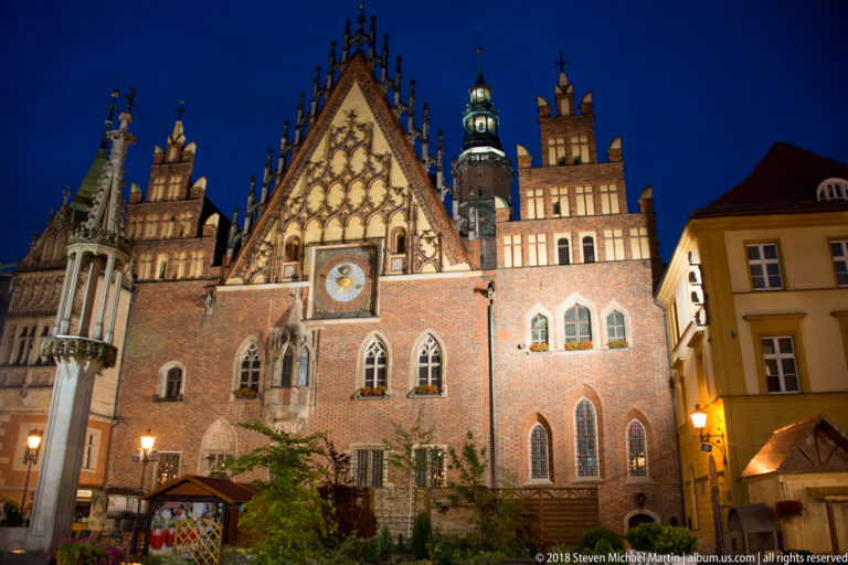 Wrocław Old Town Hall at blue hour, showing the illuminated Gothic east gable and astronomical clock.