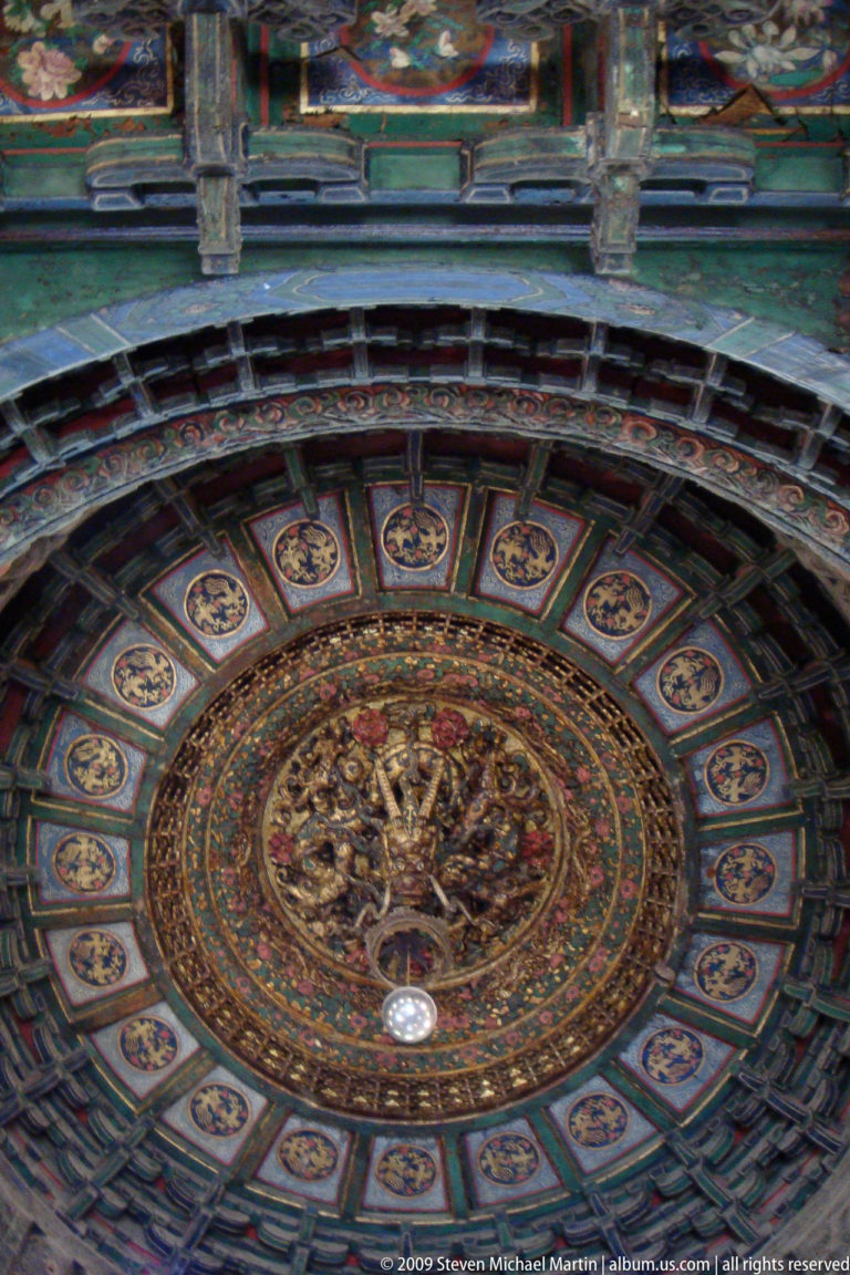 Close-up upward view of a dragon caisson ceiling with gilded dragons in a central medallion surrounded by blue-green coffers and circular dragon panels in a radial pattern.