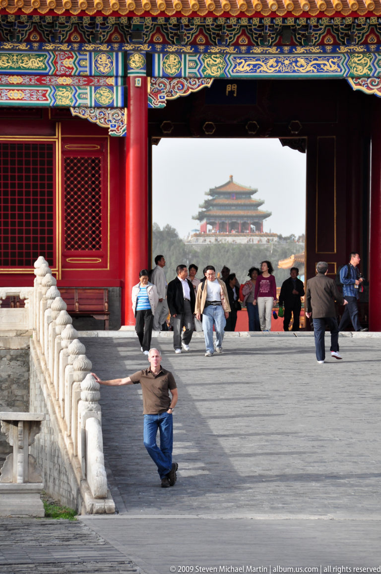 Male visitor on a crowded Forbidden City terrace with the distant Jingshan pavilion framed along the central axis.