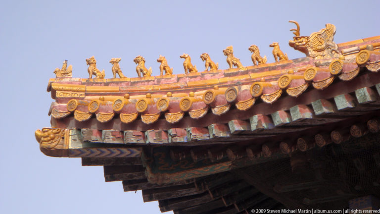 Close-up of a yellow-glazed imperial roof ridge in the Forbidden City with a procession of guardian figurines leading toward a larger corner beast.
