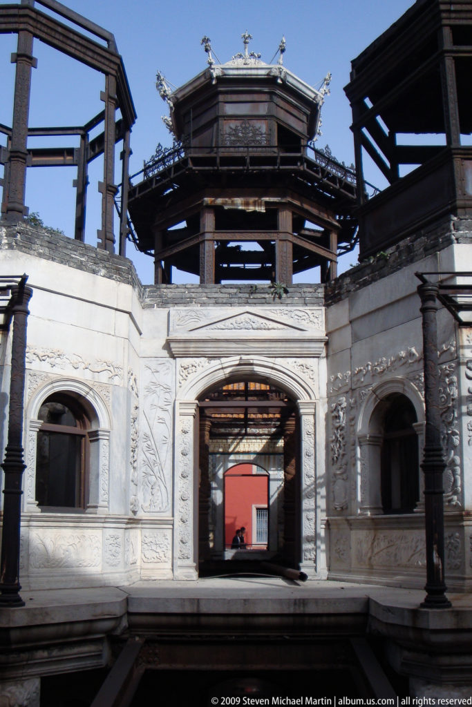 View through carved Western-style stone arches toward exposed timber framing and a partially open roof in a historic structure inside the Forbidden City.