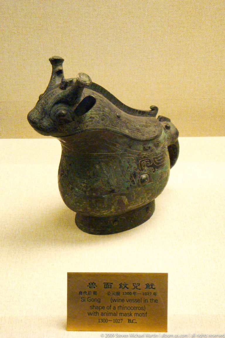 Bronze tripod jue ritual wine vessel with long spout, raised handle, and archaic-style decoration displayed as a palace-collection object.