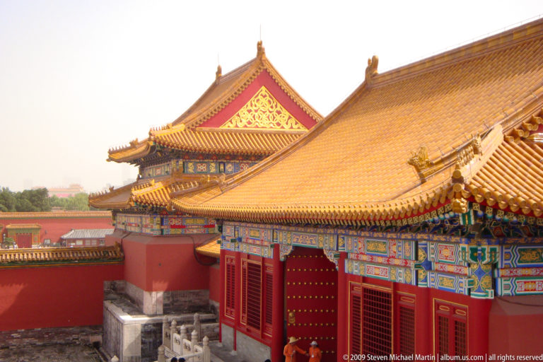 Oblique view of a red-walled palace hall in the Forbidden City with painted dougong brackets supporting sweeping yellow-glazed roof tiles.