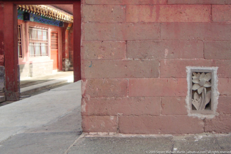 Vermilion masonry palace wall with a small pale carved stone ventilation grille near ground level.