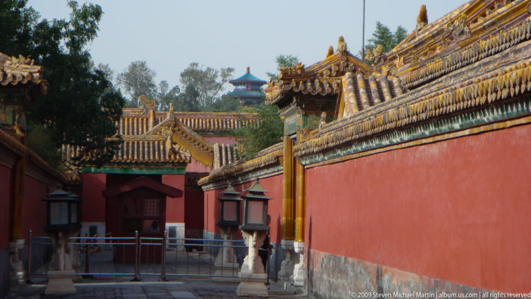 Long, narrow passage in the Forbidden City lined with tall red walls, tiled roofs, and traditional lanterns.