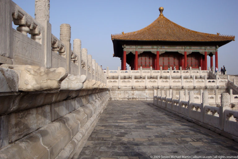 Low oblique view along a stone terrace toward an imperial hall, with carved balustrades and a projecting stone drainage spout.