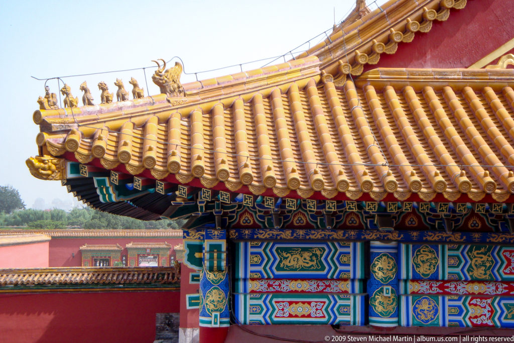 Close-up of a Forbidden City hall roof corner with yellow glazed tiles, roof ornaments, and blue-green painted bracket work under the eaves.