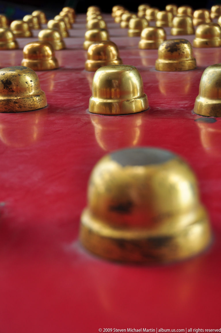 Close-up of gilded door studs on glossy vermilion red lacquer, with shallow depth of field blurring the foreground stud.