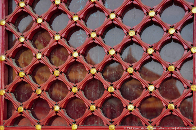 Close-up of a red diamond lattice window with small gilded rosette bosses at each intersection.