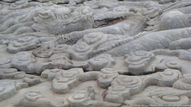Close-up of a carved stone dragon in low relief amid cloud and wave motifs on an imperial ramp in the Forbidden City.