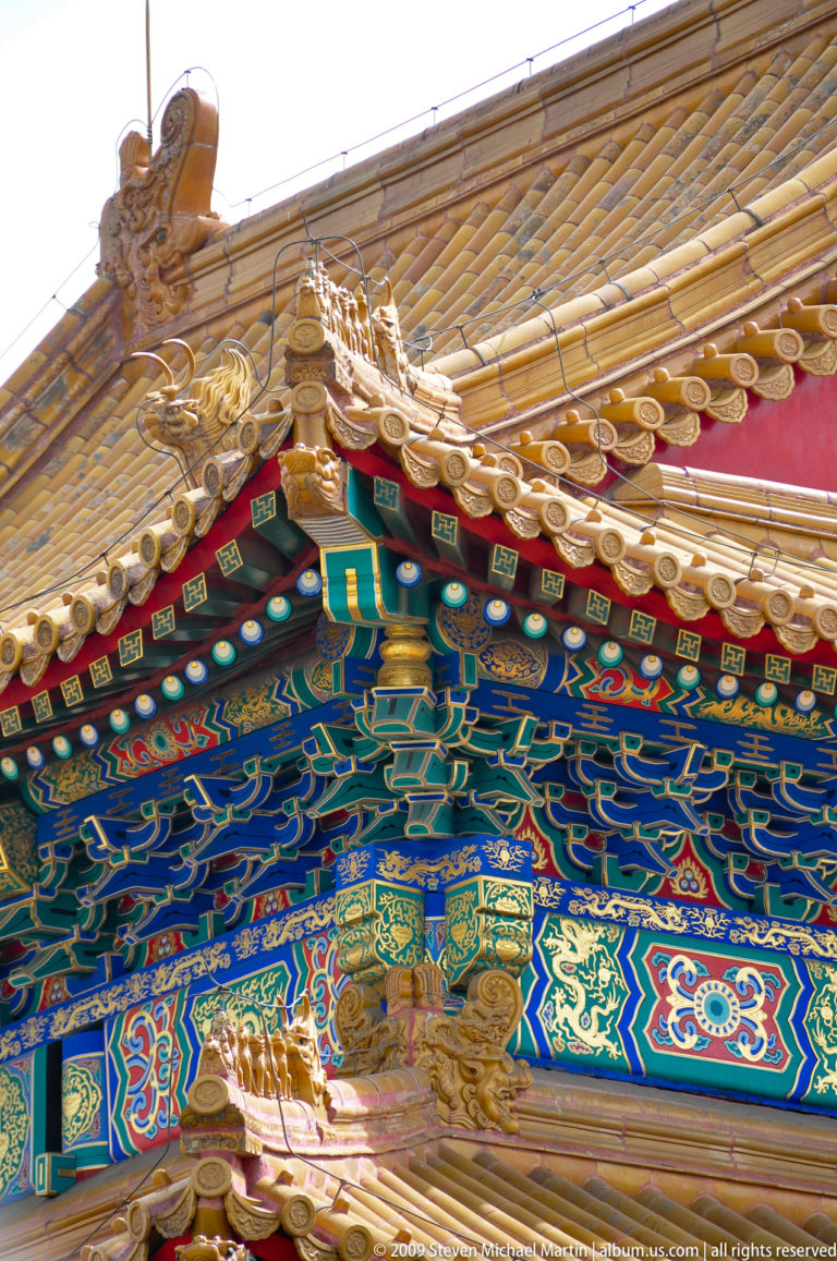 Close-up of a Forbidden City gable corner with yellow glazed tiles above densely layered, painted dougong brackets.