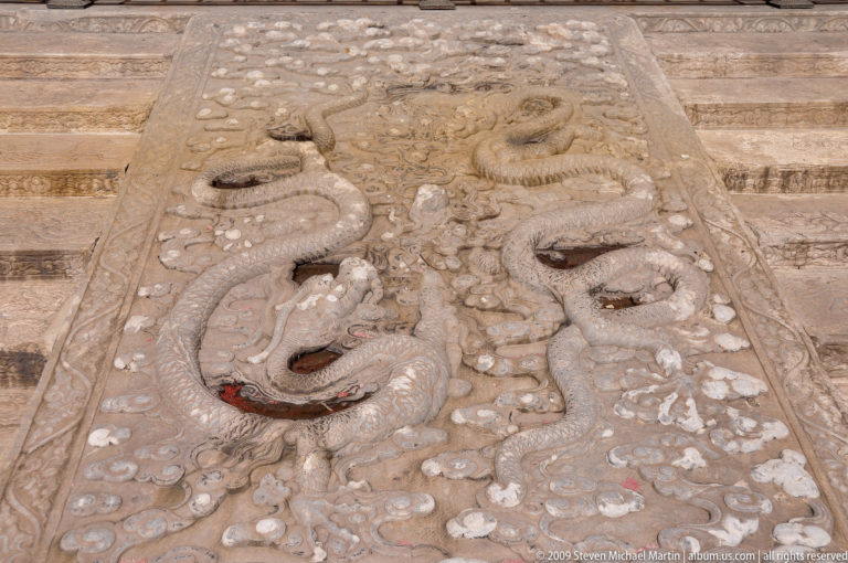 Carved stone ramp in the Forbidden City with a full dragon in relief amid cloud and wave motifs.