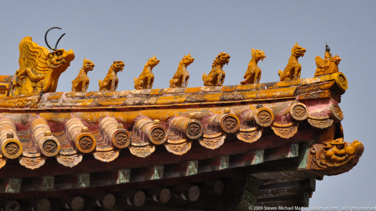 Close-up of yellow-glazed imperial roof figurines and a horned, dragon-like corner beast on a Forbidden City roof.