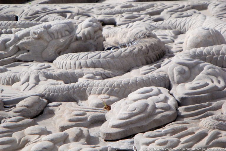 Close-up of a carved stone imperial stair ramp showing a coiled dragon amid dense cloud and wave motifs on a worn, pale surface.