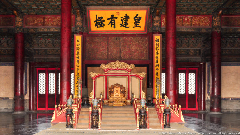 Symmetrical imperial throne room interior with an elevated throne behind red railings, red columns, ritual vessels, and a prominent plaque reading “皇建有极” above the seat.